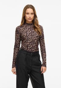 Leopard print long-sleeve top in brown and black, made of soft fabric. Features a high neck and is paired with tailored black pants.