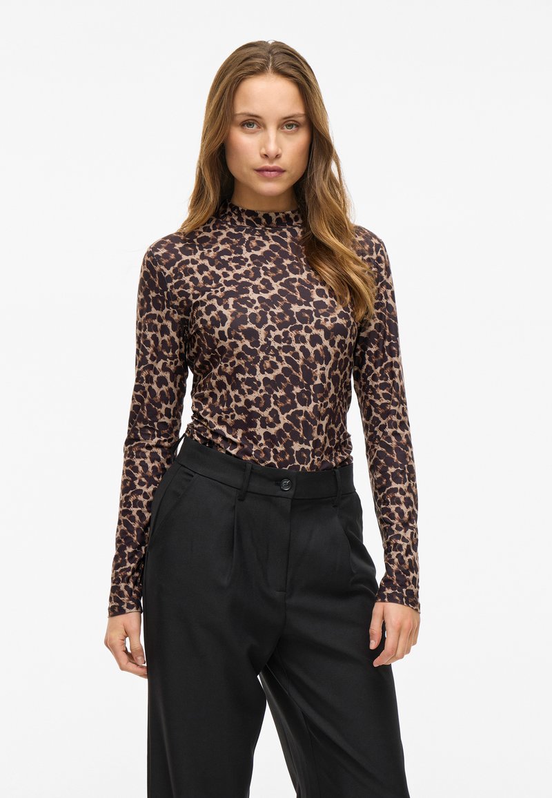 Leopard print long-sleeve top in brown and black, made of soft fabric. Features a high neck and is paired with tailored black pants.