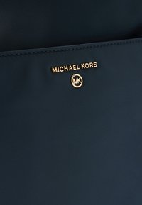 Tengerészkék nylon táska arany színű "MICHAEL KORS" logóval és kör alakú emblémával. Texturált felület sima befejezéssel.