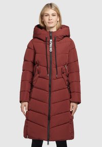 Cappotto lungo imbottito di colore rosso scuro, con un colletto alto, chiusura con zip, tasche laterali e dettaglio del logo a contrasto sul davanti.