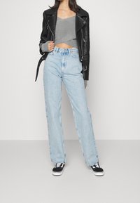 Zwarte leren motorjacket over een grijze cropped sweater, gecombineerd met lichtblauwe wide-leg spijkerbroek en zwarte sneakers met witte zolen.
