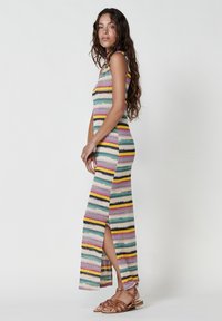 Strick-Maxi-Kleid mit vertikalen mehrfarbigen Streifen und hohem Schlitz. Das Material wirkt leicht. Das Model trägt flache Sandalen.