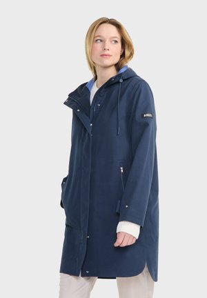Námořnická modrá nepromokavá parka s kapucí, dvěma bočními kapsami na zip a bílou podšívkou. Obsahuje nastavitelné šňůrky a patentky.