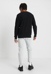 Sudadera negra de manga larga con cuello redondo, tejido texturizado y puños acanalados, combinada con jeans de mezclilla de lavado claro y zapatillas negras.