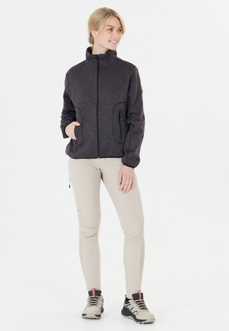 Mörkgrå zip-up fleecejacka med sidofickor, ihopparad med ljusbeiga byxor och skor med svarta detaljer och röda accenter.