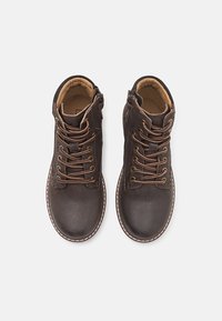 Bruine leren enkellaarzen met bruine veters, ronde neus en contrasterende stiksels. Voorzien van een zijrits voor eenvoudig aan- en uittrekken. Zachte voering aan de binnenkant.