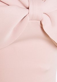 Ljusrosa tyg har ett texturerat mönster, med en stor rosett vid midjan som ger en slät och figurnära look.