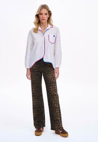 Biała koszula z różowymi i niebieskimi kontrastującymi wykończeniami, zestawiona z brązowymi spodniami w leoparda o szerokich nogawkach i brązowymi platformami.
