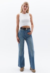 Top corto bianco, jeans blu a vita alta, cintura marrone con fibbia in argento e stivali chunky marrone chiaro. Tessuto liscio, vestibilità rilassata.