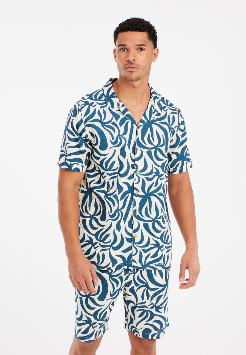 Conjunto de camisa de botón de manga corta y pantalones cortos en un patrón de hojas en azul y crema. Hecho de una tela ligera con un corte relajado y botones de madera.