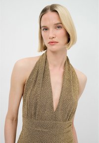 Robe à col halter en tissu métallisé doré avec un décolleté en V profond et une finition texturée. Présente des drapés fluides et une taille ajustée.