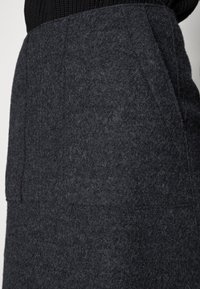 Jupe en feutre gris foncé avec une texture lisse et des lignes épurées. Elle présente deux poches latérales et une silhouette ajustée.