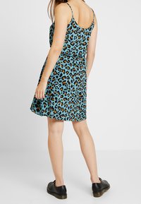 En turkos klänning med ett svart och orange leopardmönster, med figursydd midja och utsvängd kjol. Svarta skor fulländar outfiten.