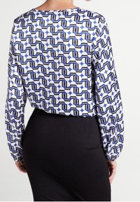 Blusa a maniche lunghe in blu, bianco e nero con motivo geometrico, dalla texture morbida e dal fit rilassato, abbinata a una gonna scura.