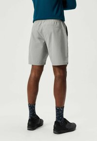 Lichtgrijze sportshorts met een elastische tailleband, een ontspannen pasvorm en zijzakken, gecombineerd met zwarte schoenen en gestreepte donkere sokken.