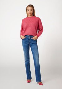 Maglione rosa a coste con scollo rotondo, abbinato a jeans blu a gamba dritta e scarpe con tacco rosa. Outfit casual e confortevole.