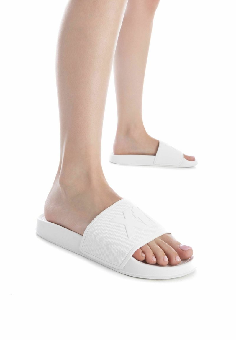 Chanclas blancas con correas anchas texturizadas, que presentan un logotipo elevado en la parte frontal. Las suelas son planas con un acabado suave.