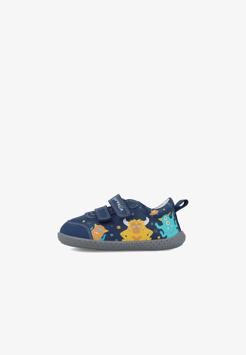 Zapato infantil azul marino con dos correas de velcro, que presenta gráficos de monstruos coloridos, suela de goma gris y un tirador en el talón reforzado.