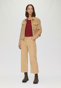 Beige corduroy jack met twee borstzakken, gecombineerd met beige corduroy broek. Rood T-shirt met ronde hals eronder, zwarte chunky boots.