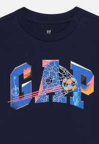 Námořnické bavlněné tričko s výrazným nápisem "GAP" a grafikou fotbalové sítě a míče v růžových, modrých a oranžových akcentoch.