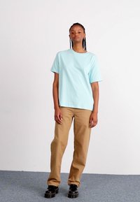 Lyseblå bomulds t-shirt med lige skæring, korte ærmer; parret med sandfarvede lige ben bukser og sorte chunky sko.
