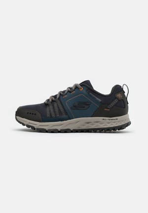 Dark blue athletic shoe with textured mesh upper, grey accents, and orange laces. Features a cushioned sole with a rugged tread.