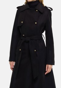 Zwarte wollen jas met een ceintuur in de taille, dubbelrijg ontwerp met gouden knopen, schouderepauletten en een brede kraag.