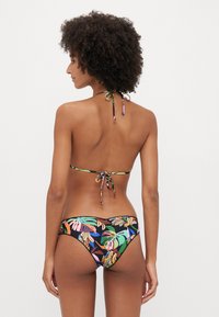 Bikini set featuring a back tie halter top and low-rise bottom with a multicolored tropical leaf pattern on a black background.