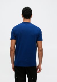 Modré bavlnené tričko s krátkymi rukávmi a okrúhlym výstrihom, s hladkou textúrou a voľným strihom. Jednoduchý dizajn bez vzorov.