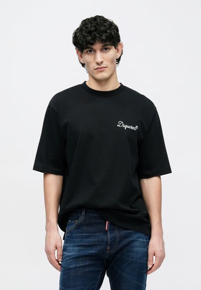 Melna kokvilnas T-krekls ar brīvu pieguļošu piegriezumu, apaļu izgriezumu un īsām piedurknēm. Uz kreisā krūškurvja ir balts "Dsquared2" logotips.