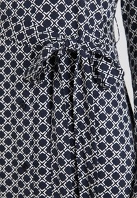 Abito navy con un motivo geometrico bianco, vita con cintura e fiocco, e dettagli con bottoni, realizzato in un tessuto morbido con una leggera texture.