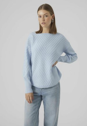 Maglione a maglia azzurro chiaro con motivo a zig zag, ampia scollatura a barca e polsini a costine. Abbinato a jeans in denim chiaro.