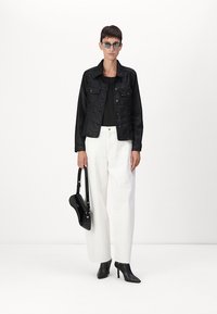 Giacca di jeans nera con due tasche sul petto, abbinata a un top nero aderente e pantaloni bianchi larghi. Borsa nera e stivali con tacco a punta.