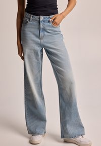 Vaqueros acampanados de un azul claro, confeccionados en denim con un acabado deslavado, con cintura alta, bolsillos laterales y costuras en contraste.