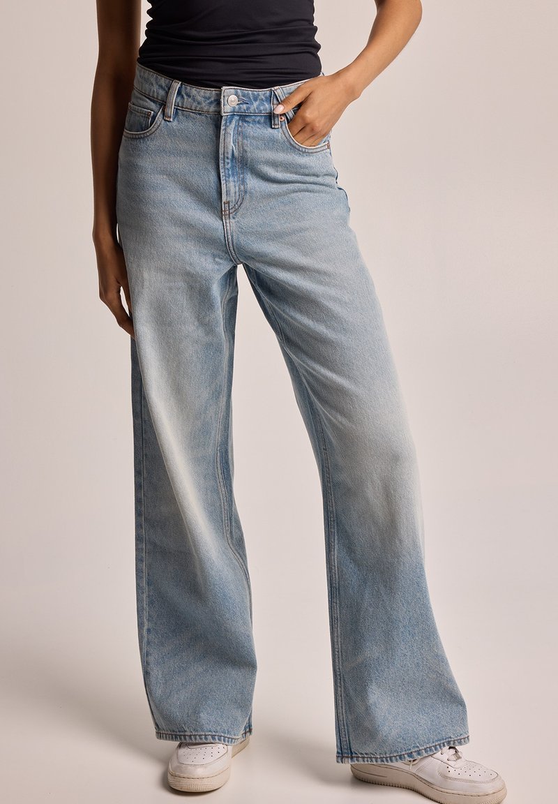 Vaqueros acampanados de un azul claro, confeccionados en denim con un acabado deslavado, con cintura alta, bolsillos laterales y costuras en contraste.