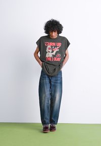 Tmavě zelené oversized tričko s grafickým potiskem, spárované se volnými modrými džíny a hnědými botami. Jednoduchý design, pohodlný střih.