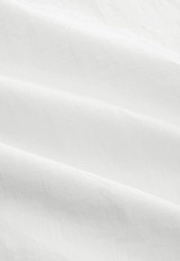 Tessuto bianco con morbide pieghe e una sottile trama, illuminato dalla luce naturale.