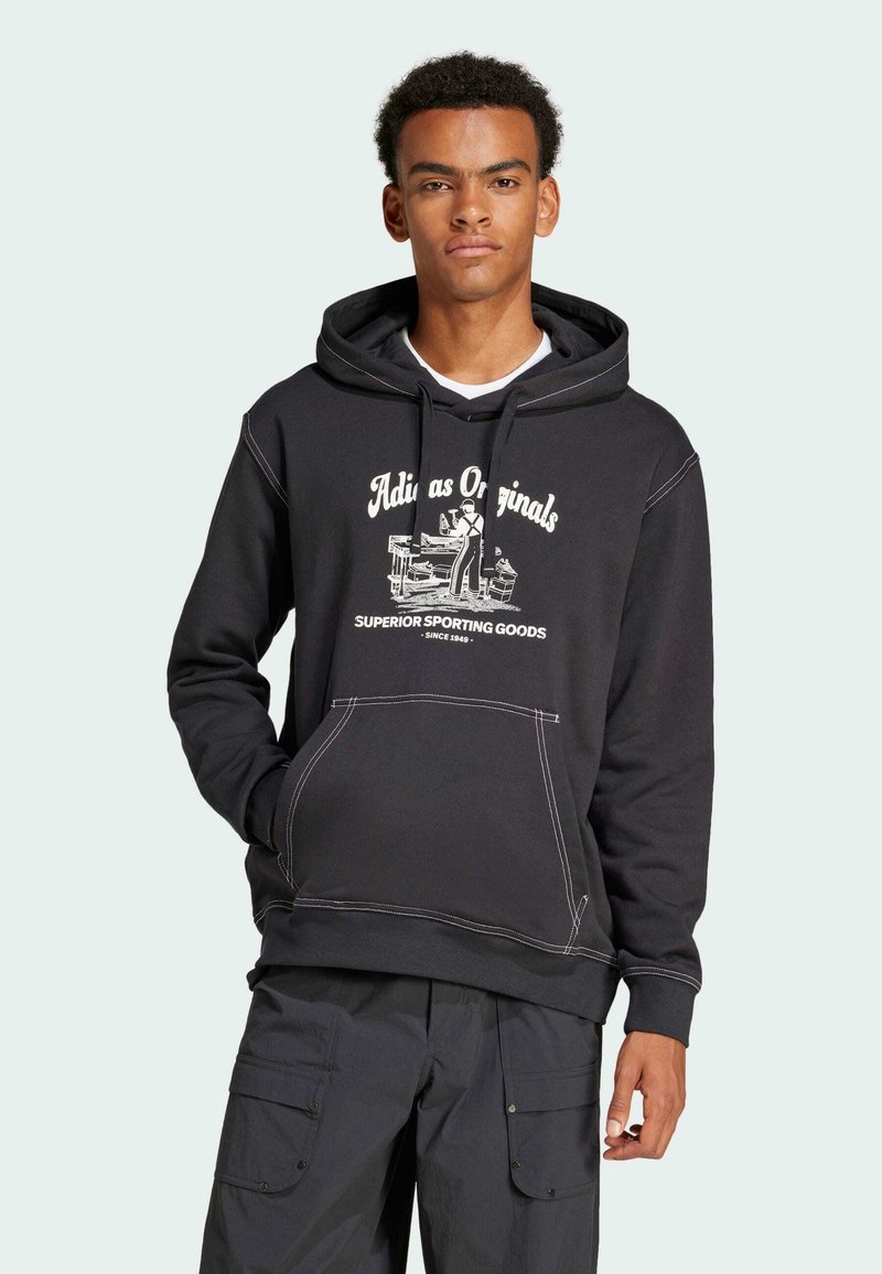 Zwarte hoodie met witte grafische print met tekst en een figuur. Contraststiksels. Voorzakdetail. Gemaakt in combinatie met grijze cargobroek.