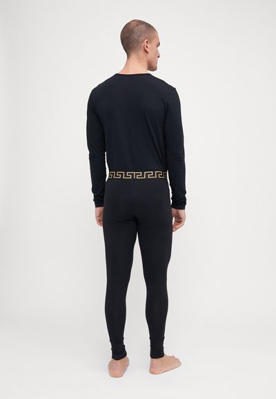 Långärmad svart topp och figurnära svarta leggings med ett guldigt grekiskt nyckelmönster i midjan. Tygmaterialet verkar slätt och elastiskt.