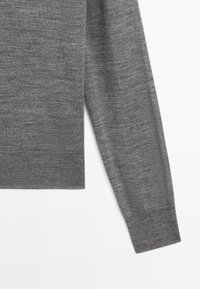 Szary sweter wykonany z miękkiej dzianiny, z okrągłym dekoltem, długimi rękawami oraz ściągaczami na mankietach i dole. Gładka faktura z jednolitym wzorem.