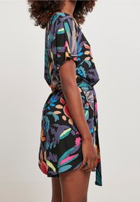 Flerfärgad blommig klänning i lätt tyg, med korta ärmar och knytning i midjan, med svart bakgrund och livfulla accenter.