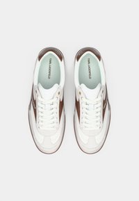 Ζευγάρι λευκών και καφέ αθλητικών παπουτσιών Karl Lagerfeld με κορδόνια, σε θέα από πάνω σε λευκό φόντο.