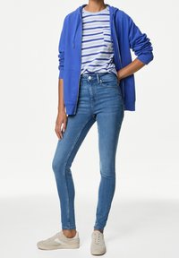 Sudadera azul con cremallera, camiseta a rayas con bolsillo, jeans ajustados azules y zapatillas ligeras. Enfoque en texturas suaves y diseño casual.