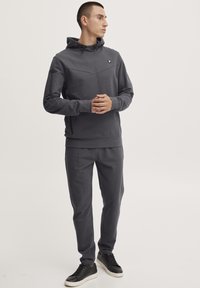 Grå hettegenser med frontlogo, kombinert med matchende grå joggebukser. Glatt tekstur, minimalistisk design og strømlinjeformet fasong.