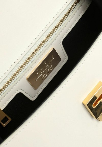 Intérieur d'un sac à main en cuir blanc avec une fermeture éclair dorée, une doublure en tissu noir et une plaque logo dorée avec un texte en relief.