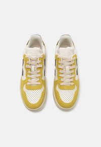 Yellow and white sneakers with a perforated toe box, beige laces, and black accents. Features a textured suede finish and rubber sole.