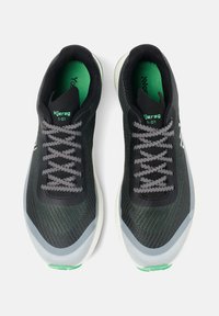 Zwarte sportieve schoenen met een getextureerde mesh bovenkant, grijze veters en groene accenten. Heeft een ronde neus en een witte tussenzool.