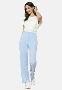 Svetlo modri hlače širokega kroja z gladko teksturo, z visokim pasom in zanko za pas, v kombinaciji z enostavno belo majico in športnimi copati.