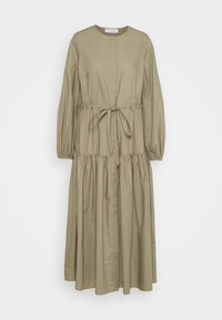 Longue robe vert olive avec manches longues, taille froncée avec ceinture, col rond et jupe à volants qui tombe droit.