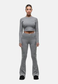 Top corto a costine grigio e pantaloni a vita alta svasati con cuciture a contrasto, dotati di tasca laterale con zip. Il modello indossa calzature nere.
